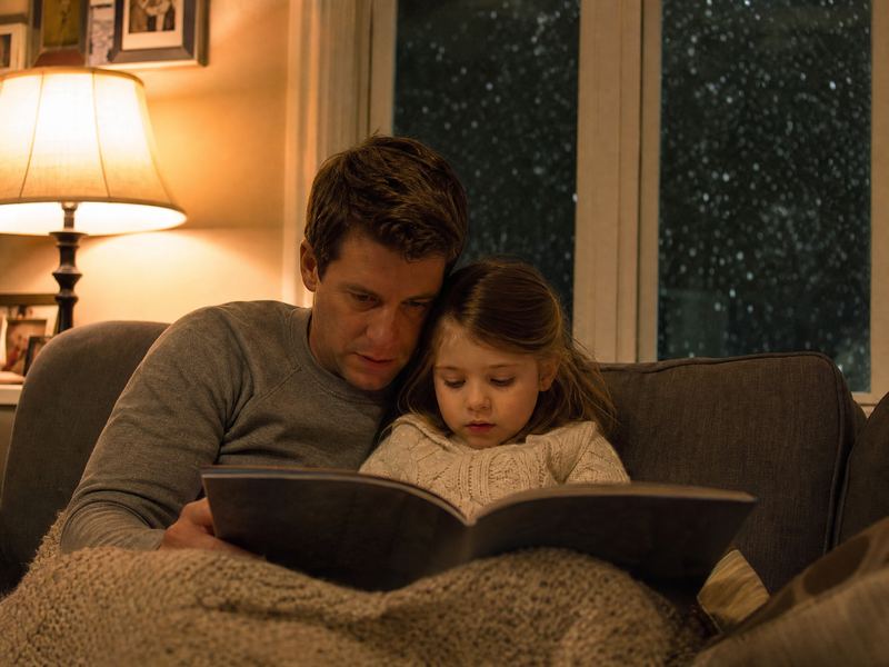 A father and daughter reading under a blanket on a winter evening